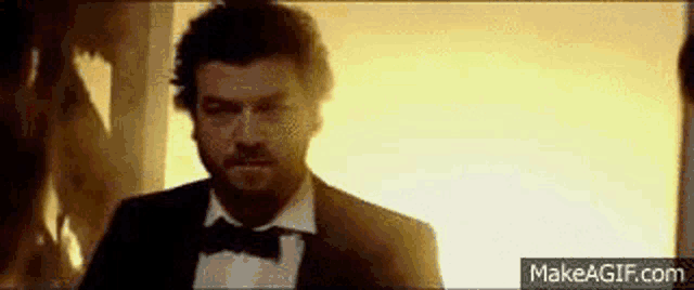 a man in a tuxedo and bow tie is standing in front of a wall .