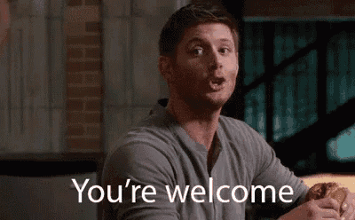 a man is sitting at a table holding a hot dog and a sign that says `` you 're welcome '' .