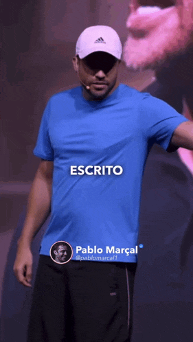 a man wearing a blue shirt and a white hat is standing in front of a microphone with the word escrito above him