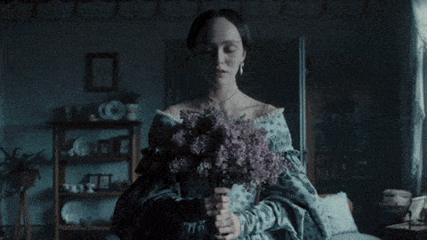 a woman is holding a bouquet of purple flowers in a dark room