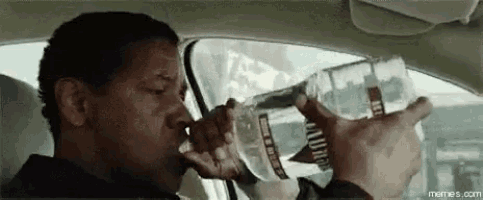 a man is drinking water from a glass while driving a car .