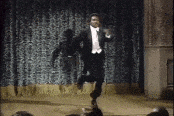 a man in a tuxedo is jumping in the air on a stage .