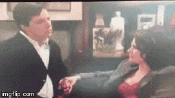 a man in a tuxedo and a woman in a red dress are sitting on a couch holding hands .