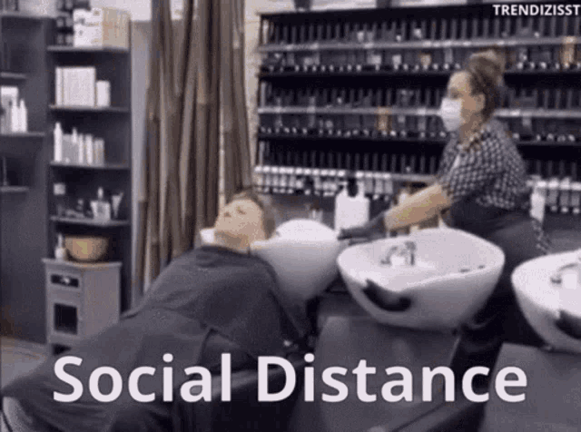 a woman is getting her hair washed in a salon with the words " social distance " on the bottom