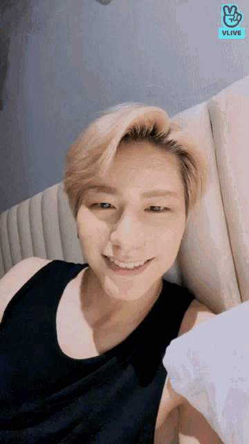 a man in a black tank top is laying on a bed with a vlive logo behind him