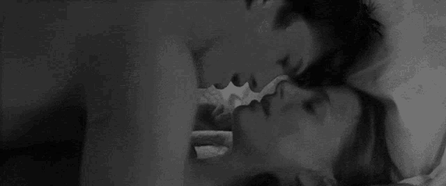 a black and white photo of a man and a woman kissing in bed .