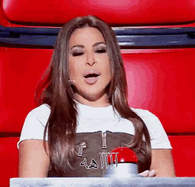a woman in a white shirt is sitting in a red chair with her mouth open
