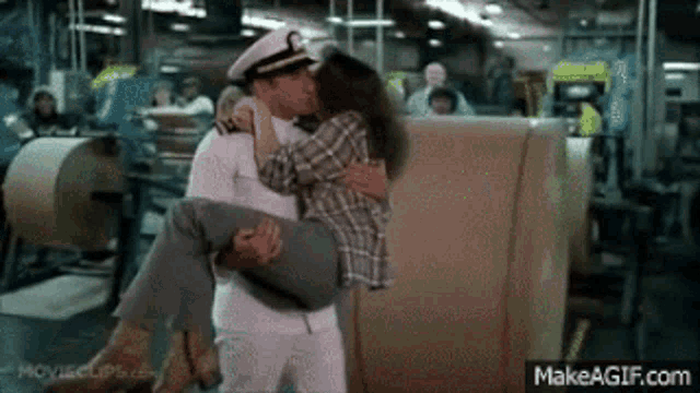 a man in a sailor hat is carrying a woman in his arms and kissing her .