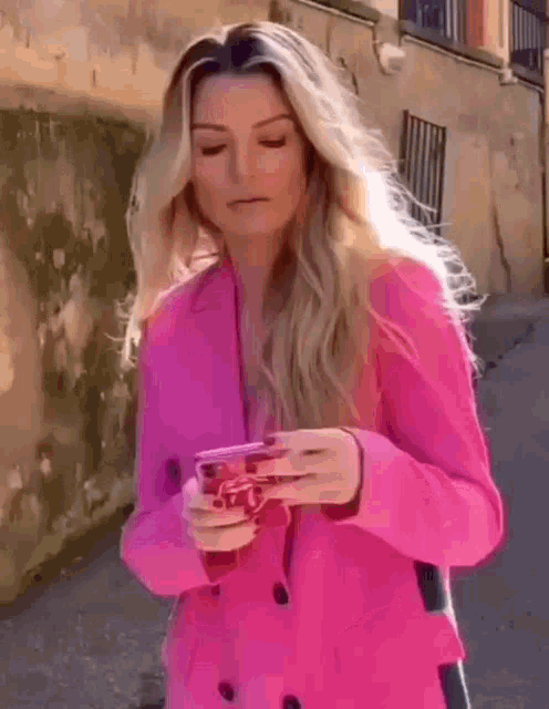 a woman wearing a pink coat is holding a cell phone .