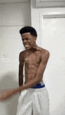 a shirtless young man in white shorts is standing in front of a white door .
