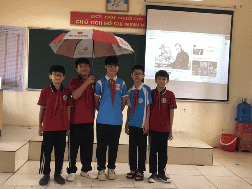 a group of young boys are standing in front of a projector screen with a sign above them that says doi doi nho on