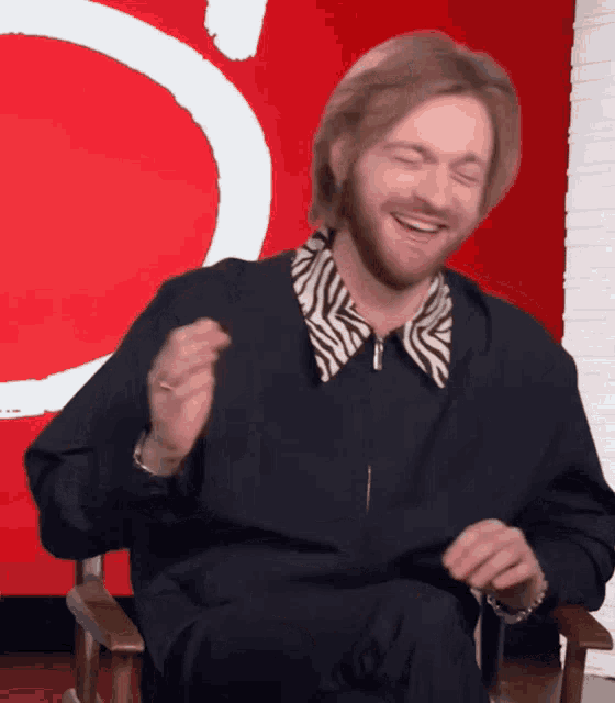 a man with a beard wearing a black jacket and a zebra print shirt is smiling