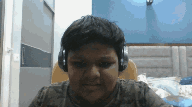 a boy wearing headphones and a camo shirt looks at the camera