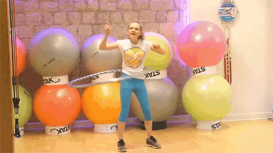 a girl is playing with a hula hoop in a gym surrounded by star branded balls