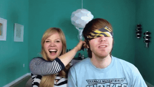 a man wearing a teenage mutant ninja turtles shirt is being blindfolded by a woman