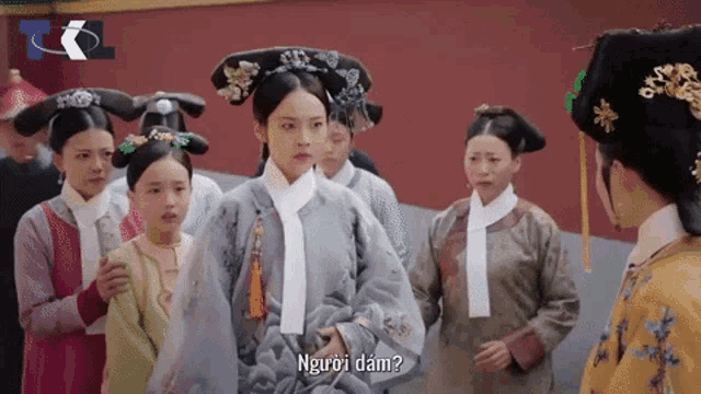 a group of asian women are standing in front of a red wall and one of them says " người dám "