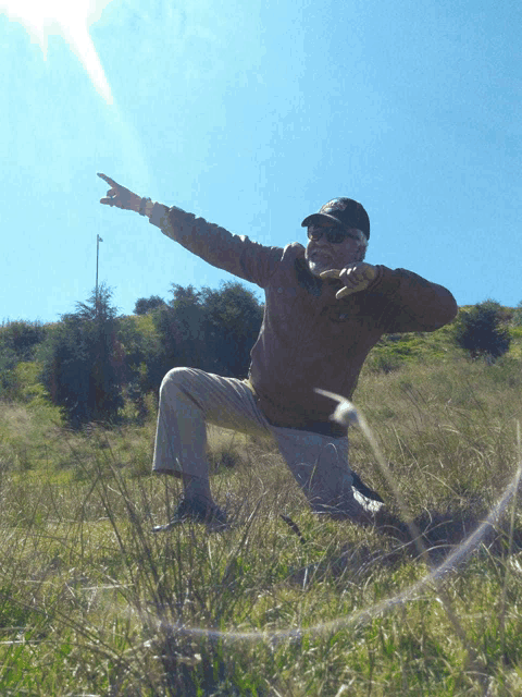 a man wearing a hat and sunglasses is kneeling in a field and pointing