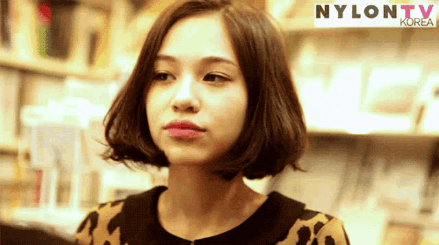 a woman with short hair stands in front of a sign that says nylontv korea