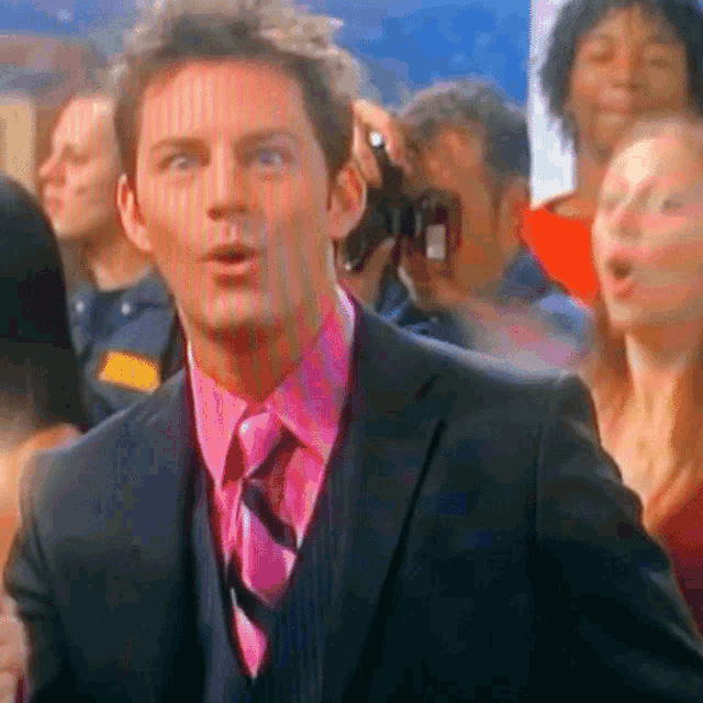 a man in a suit and pink shirt is standing in a crowd of people