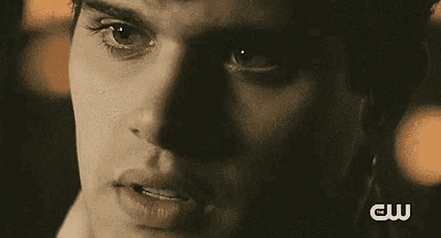 a close up of a man 's face with a blurred background and a cw logo in the corner .