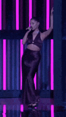 ariana grande is singing into a microphone while wearing a purple crop top and black skirt .