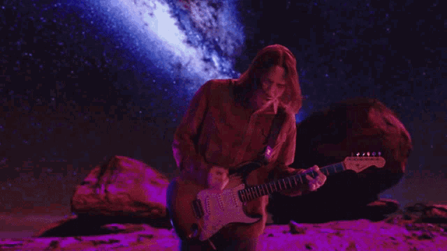 a man playing a guitar in front of a starry night sky