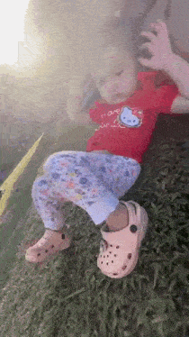 a little girl is laying on her back in the grass wearing crocs .