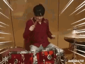 a man in a red shirt is playing drums with a microphone .