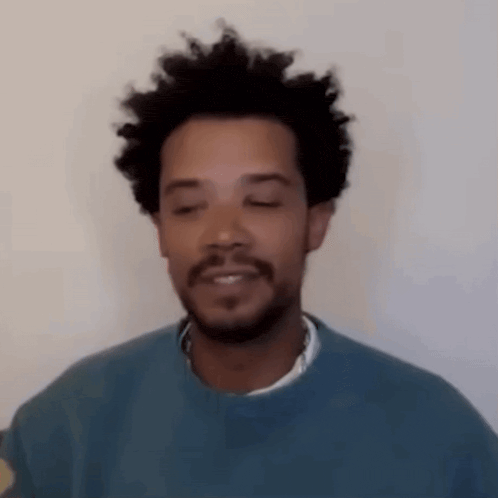 a man with a beard and curly hair is wearing a blue sweater and smiling with his eyes closed .