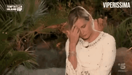 a woman in a white dress is covering her eyes with her hand .