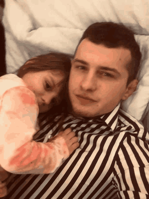 a man in a black and white striped shirt is laying on a bed with a little girl
