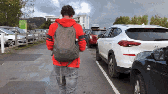 a man with a backpack walks through a parking lot with cars parked behind him