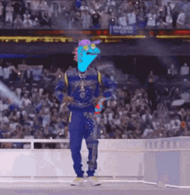 a man with a chameleon head is dancing in front of a crowd at a stadium