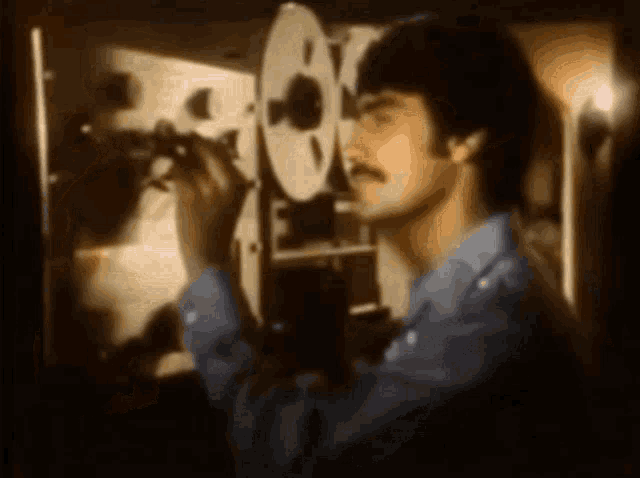 a man with a mustache is looking through a camera lens