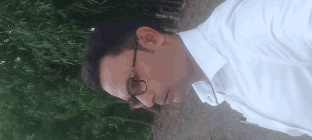 a man wearing glasses and a white shirt is standing in front of trees