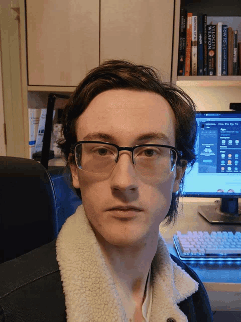 a man wearing glasses is sitting in front of a computer with a book titled velocity weapon behind him