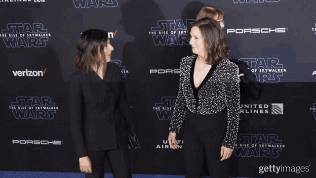 two women are standing on a red carpet that says star wars on it