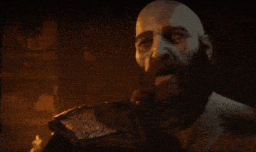 a bald man with a beard holds his hand to his face