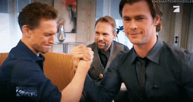three men are standing next to each other in a room and shaking hands .