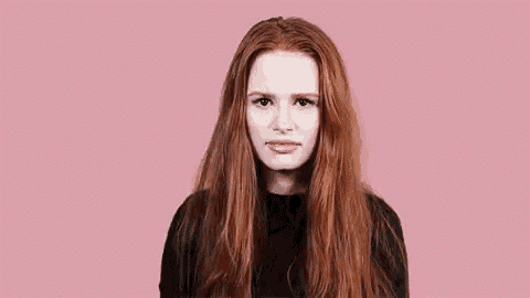 a woman with long red hair and a black shirt is making a funny face on a pink background .