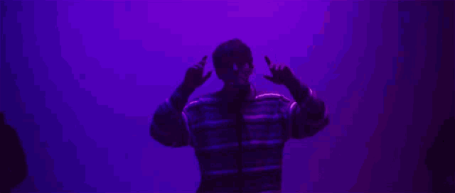 a man in a striped shirt is making a devil horns sign with his hands in front of a purple wall .