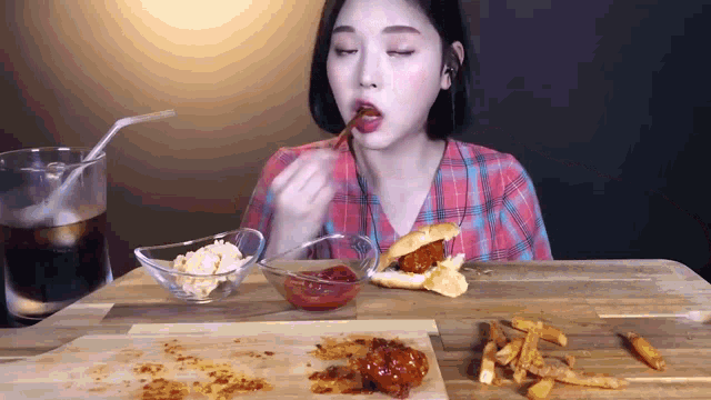 a woman in a plaid shirt is eating a sandwich and french fries at a table