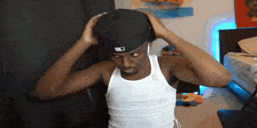 a man wearing a hat and a white tank top is adjusting his hat .