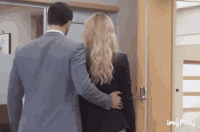 a man in a suit is holding a woman 's back while walking through a doorway .