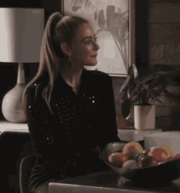 a woman sitting at a table with a bowl of fruit on it