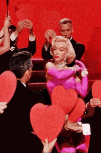 a woman in a pink dress and gloves is surrounded by people holding red hearts