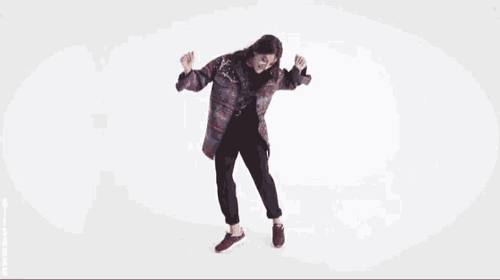 a woman in a plaid jacket and black pants is dancing on a white background