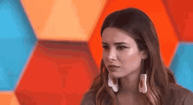 a woman wearing earrings is looking at the camera in front of a colorful wall .
