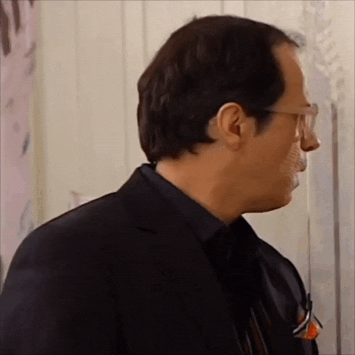 a man wearing glasses and a black suit is looking at something .