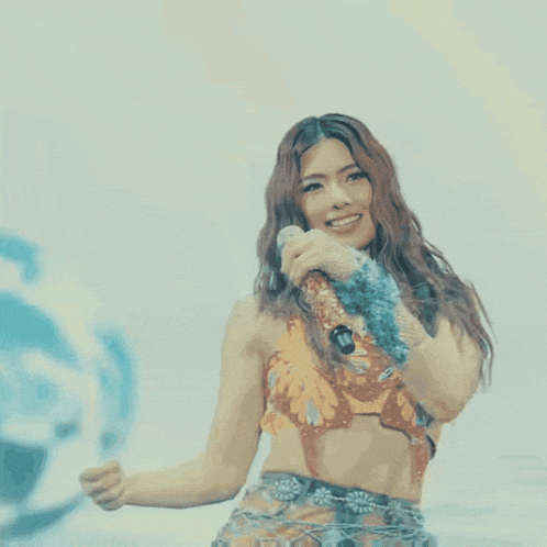 a woman singing into a microphone while wearing a crop top and skirt